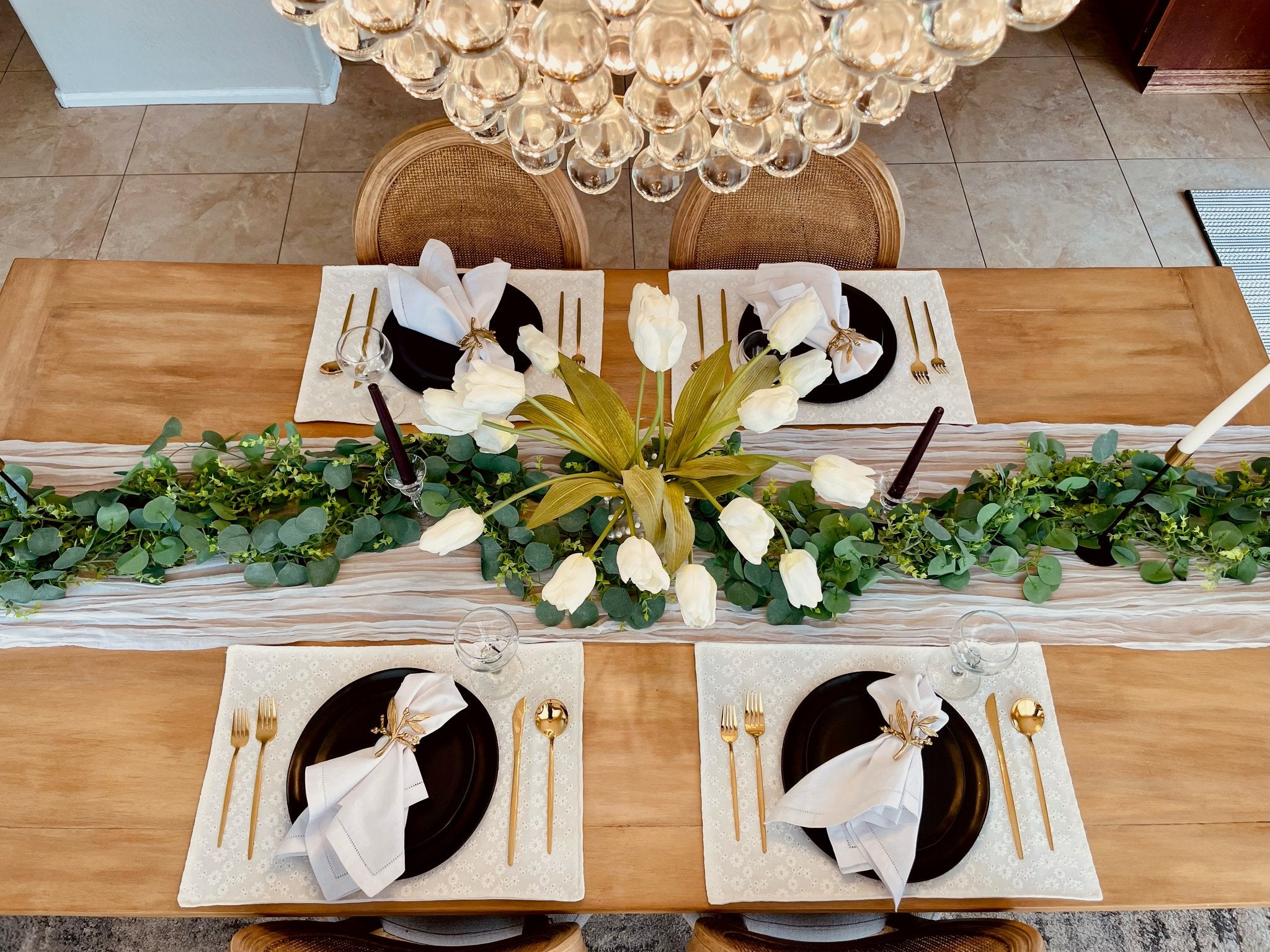 Overhead view of a dining table set for four with artificial eucalyptus garland and white tulips as a centerpiece.