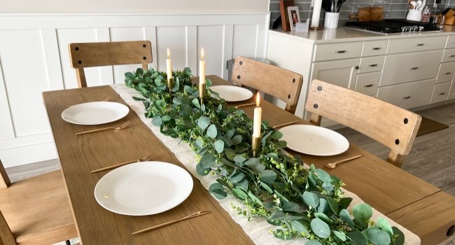 Artificial eucalyptus garland with candles and place settings on a dining table