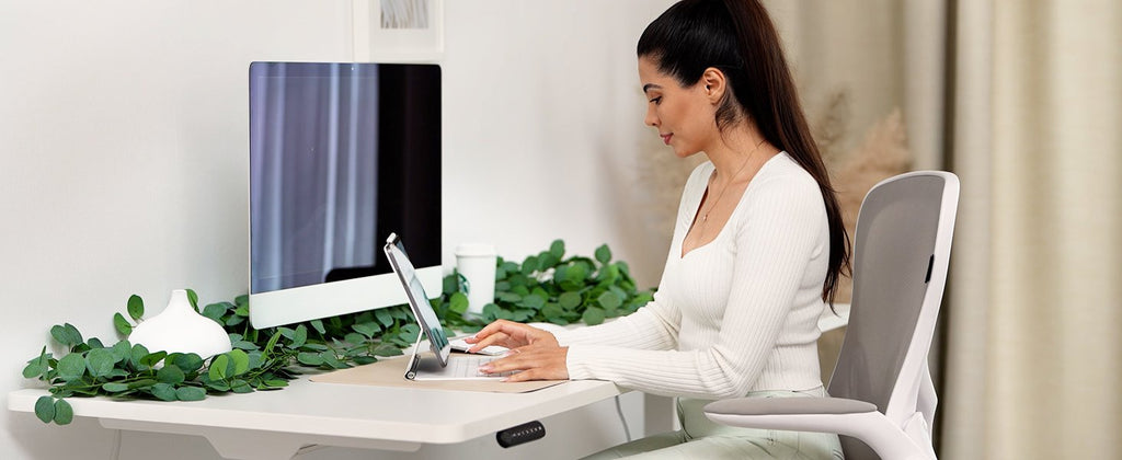 Woman working at a desk decorated with artificial eucalyptus garland and a white vase.