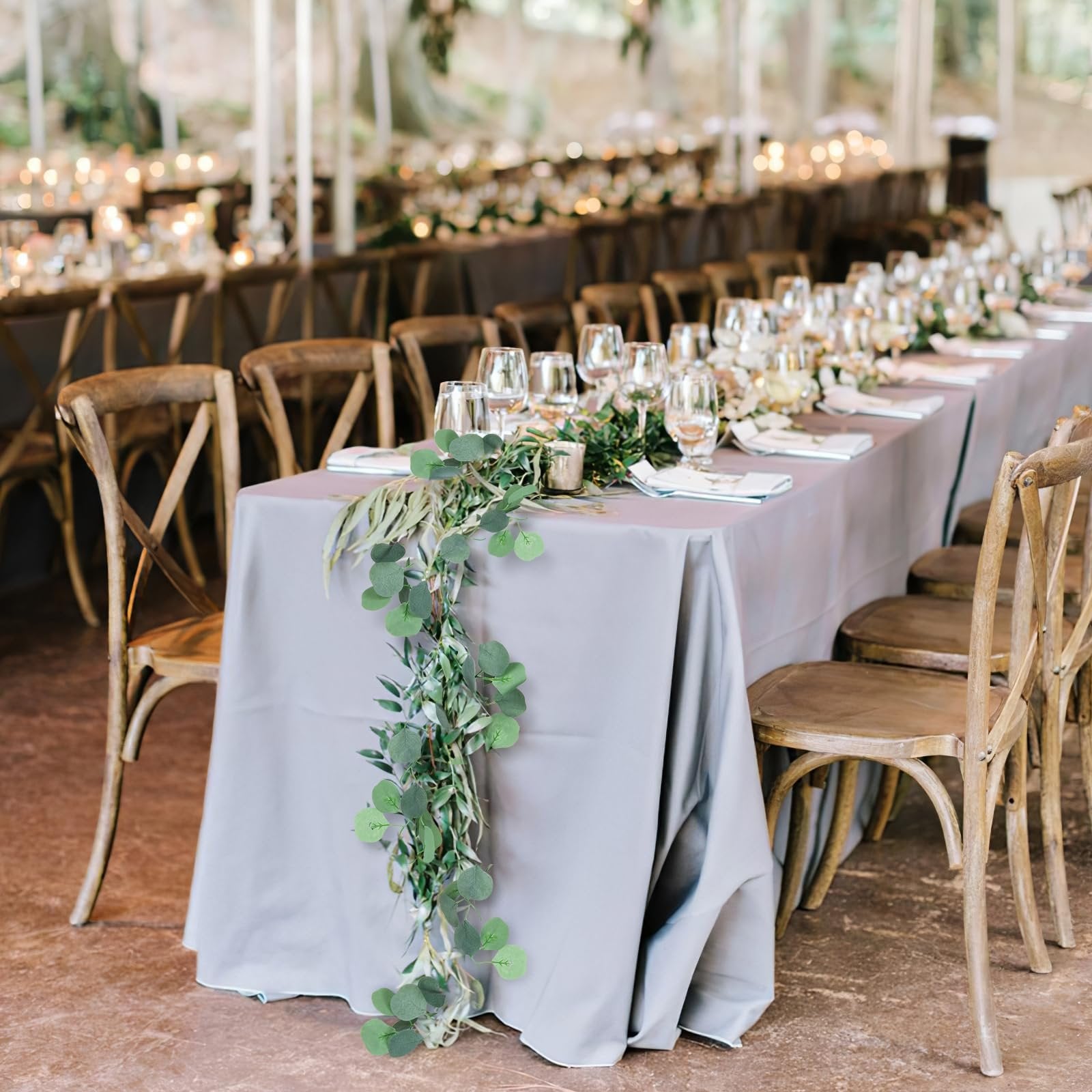 Artificial eucalyptus garland draped on a long table set for a formal event with chairs and glassware.