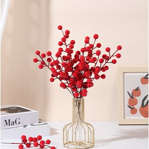 Three artificial red berry stems in a gold wire vase, with a single stem on the table and a framed picture in the background.