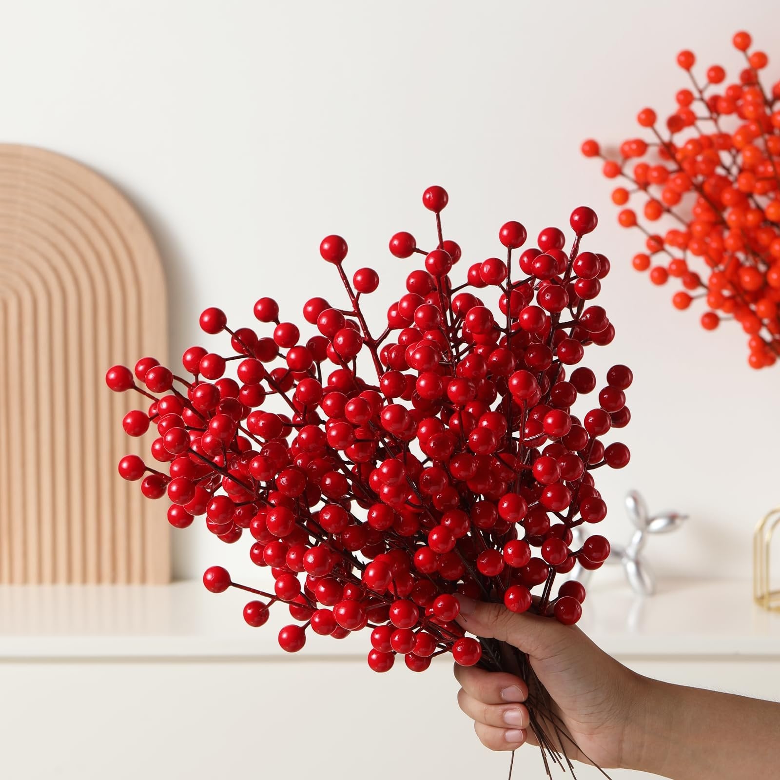 Hand holding artificial red berry stems with a blurred background of more berry stems and decor