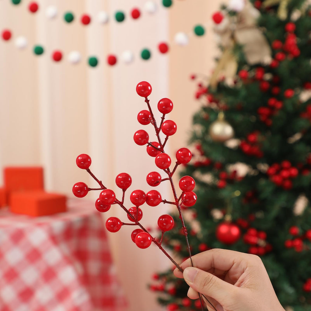 Hand holding artificial red berry stems with a blurred Christmas tree and red gift boxes in the background