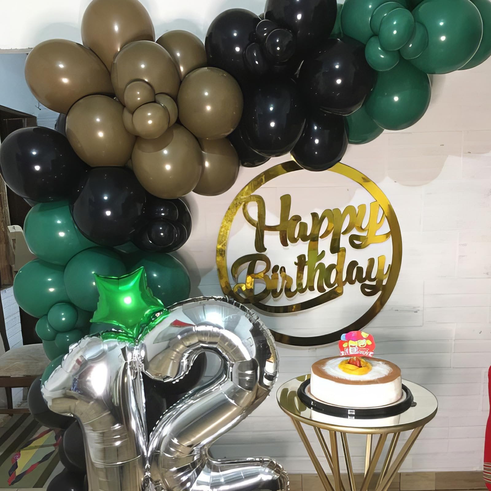 Birthday party setup with camouflage balloons, silver number balloons, and a cake on a gold table.