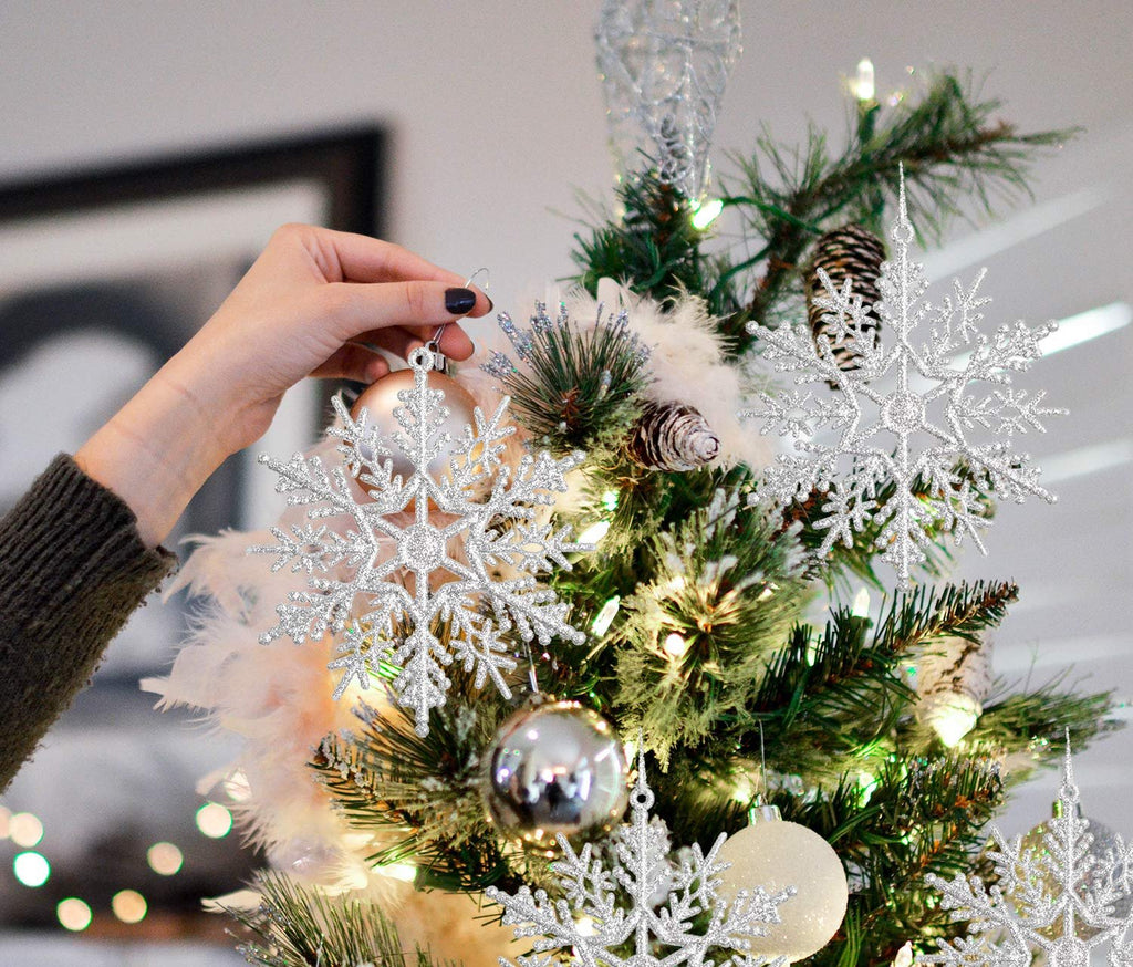 Hand decorating a Christmas tree with glitter snowflake ornaments and silver baubles