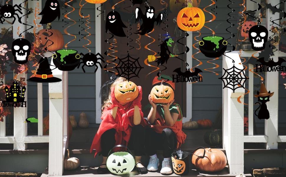 Two children in Halloween costumes sit on porch steps decorated with hanging swirl decorations, pumpkins, and a black cat.