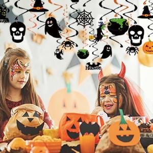 Two children with Halloween face paint sit at a table with pumpkin decorations, under hanging Halloween swirl decorations.