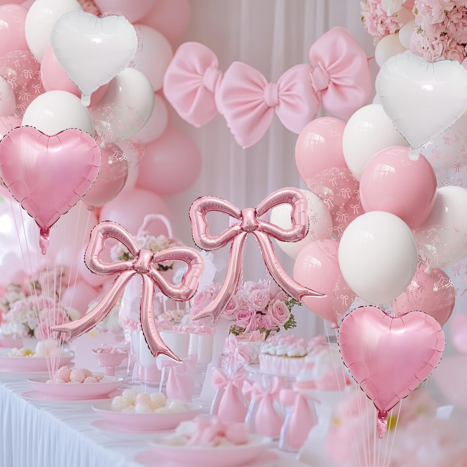 Pink and white heart and bow balloons arranged for a party setting with cakes and desserts.