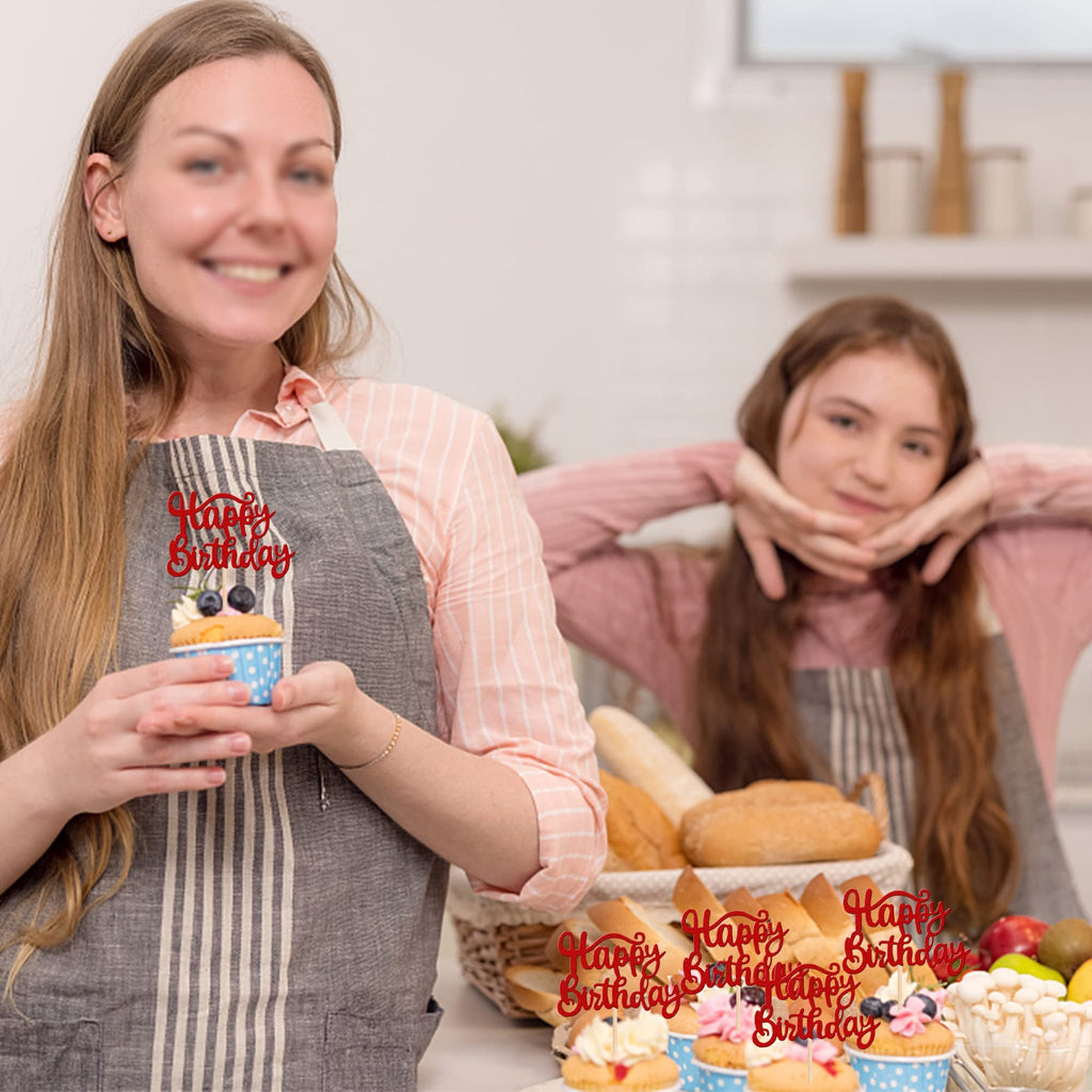 Woman holding a cupcake with a red 'Happy Birthday' topper, with a girl in the background and more cupcakes and bread.