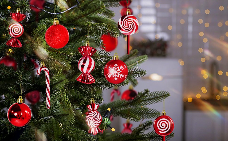Red and white Christmas ornaments in ball, candy, and lollipop shapes hanging on a decorated tree with bokeh lights in the background.