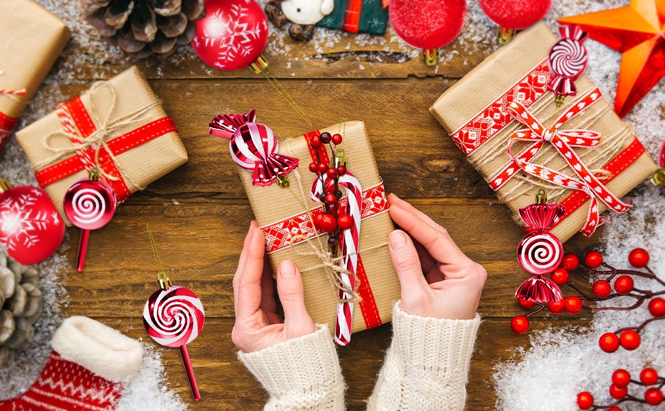 Hands holding a Christmas gift wrapped in brown paper with red ribbon and ornaments, surrounded by festive decorations.