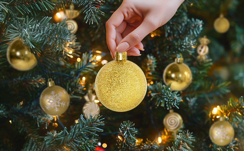Hand placing a glittery gold Christmas ornament on a decorated tree with warm lights.