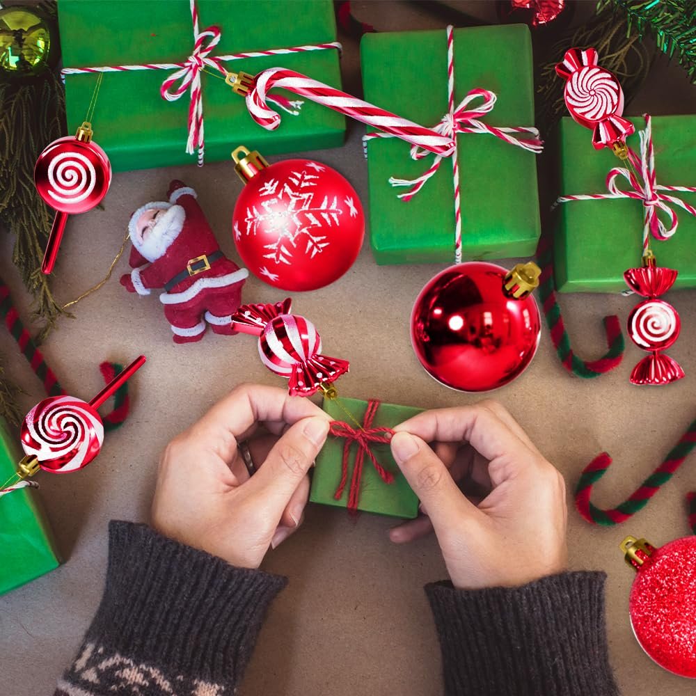 Hands wrapping a small green gift box surrounded by red and white Christmas ornaments, candy canes, and green wrapped presents.