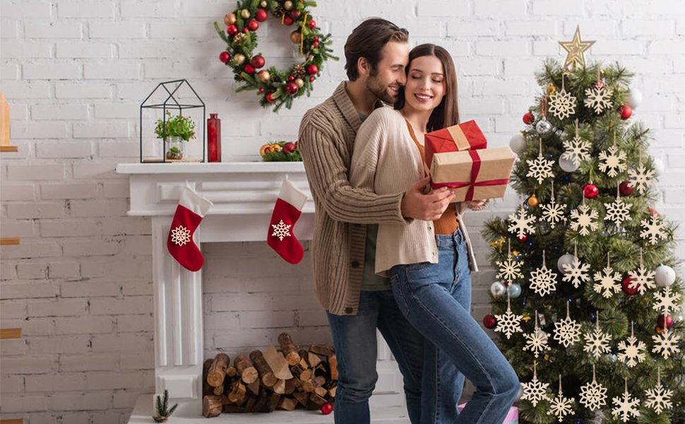 Couple embracing by a decorated Christmas tree with wooden snowflake ornaments and stockings on a fireplace