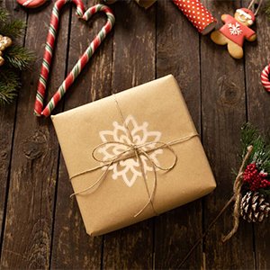 Brown paper wrapped gift box with snowflake design and jute twine, surrounded by Christmas decorations on a wooden table.