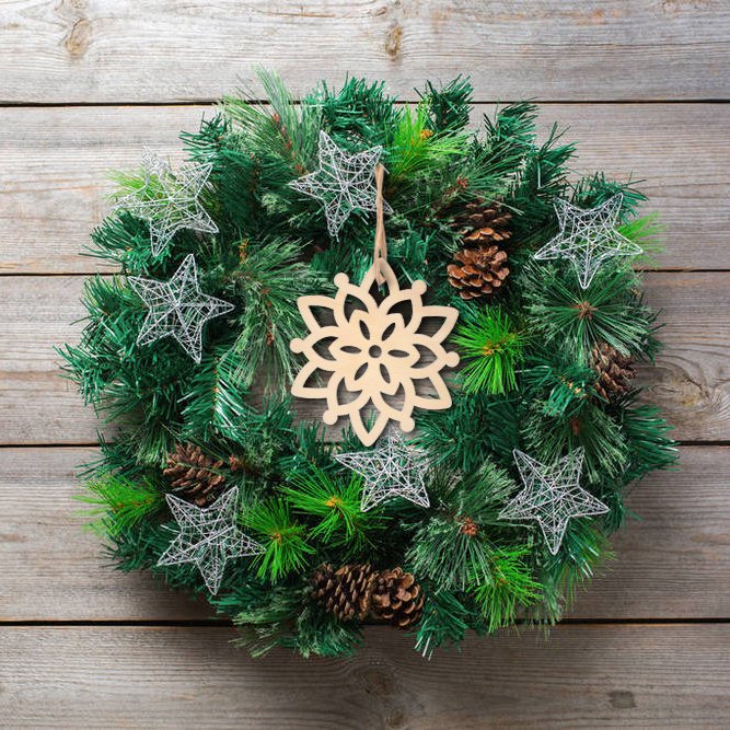 Unfinished wooden snowflake ornament hanging on a Christmas wreath with pinecones and wire stars.