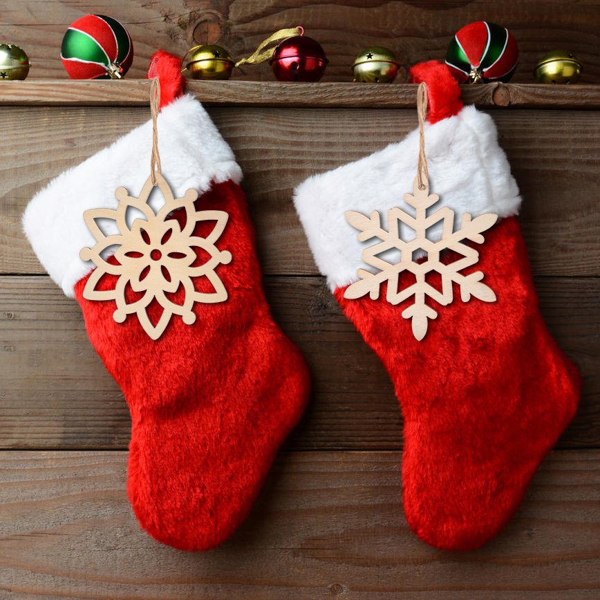 Two red Christmas stockings hang on a wooden wall, each with a wooden snowflake ornament attached.