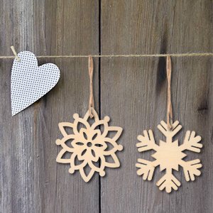 Three unfinished wooden Christmas ornaments, two snowflakes and one heart, hanging on a string against a wooden background.