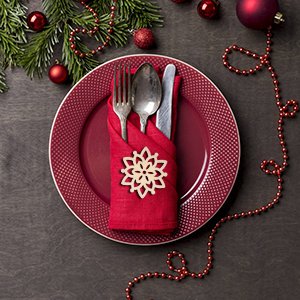 Christmas table setting with red plate, red napkin, silverware, and a wooden snowflake ornament