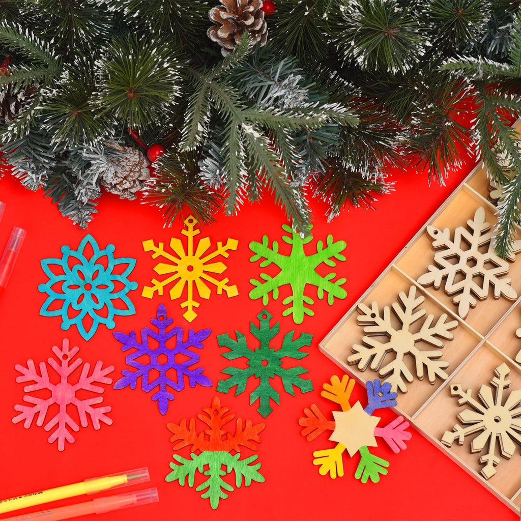 Unfinished wooden snowflake ornaments in various colors and natural wood, arranged with pine branches and markers on a red background.