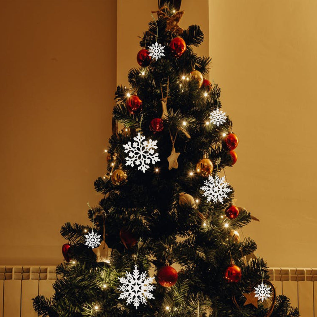 White glitter snowflake ornaments hanging on a decorated Christmas tree with warm lights.