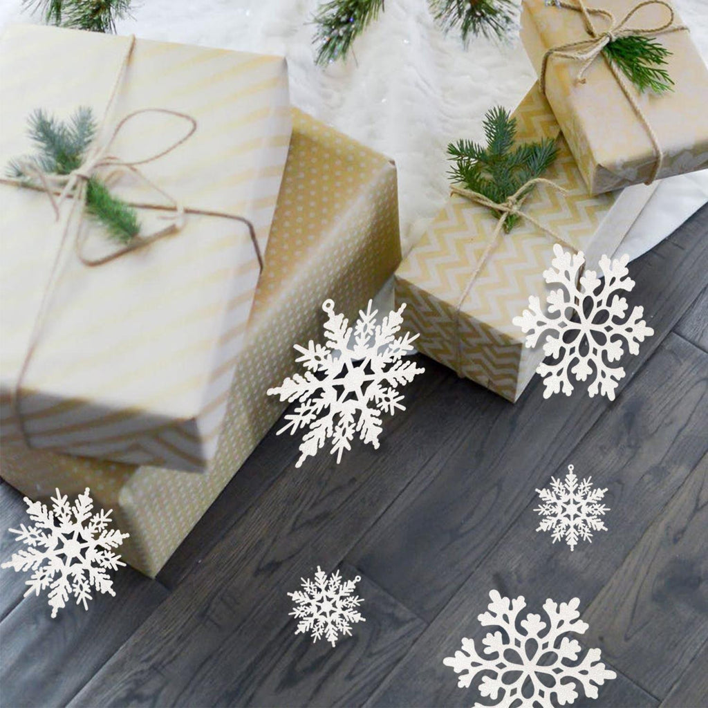 White glitter snowflake ornaments scattered on a wooden floor near wrapped Christmas gifts and pine branches.