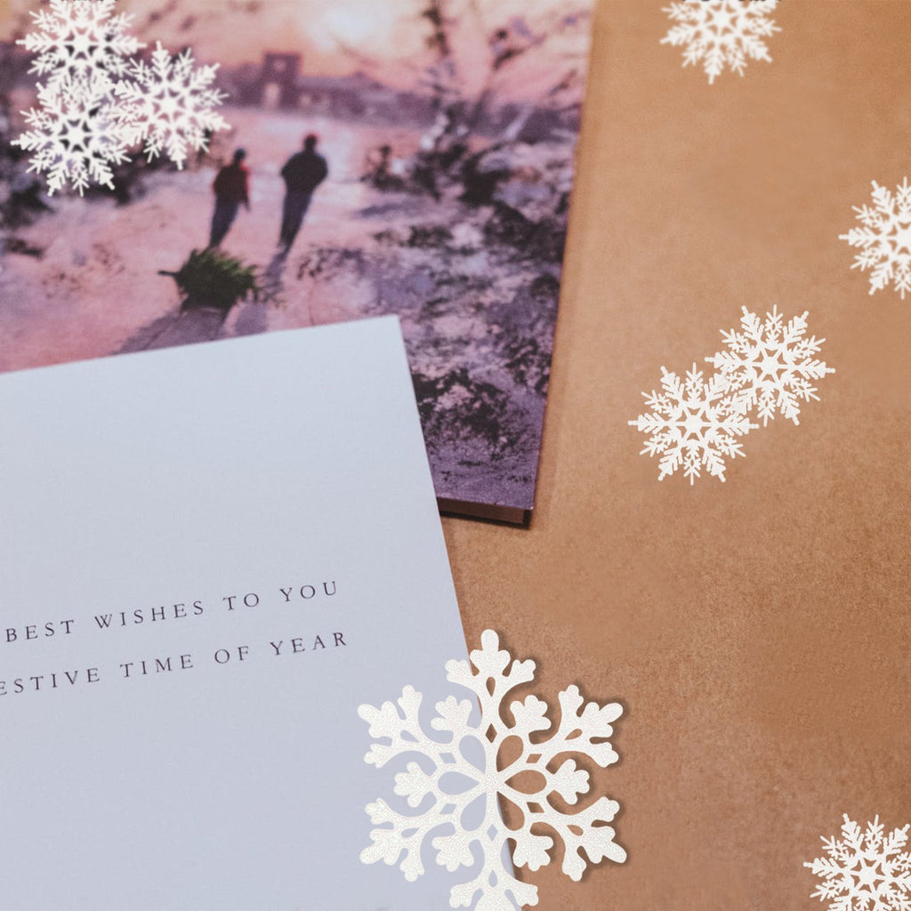 Christmas card with snowflakes and a winter scene, showing two people pulling a Christmas tree.