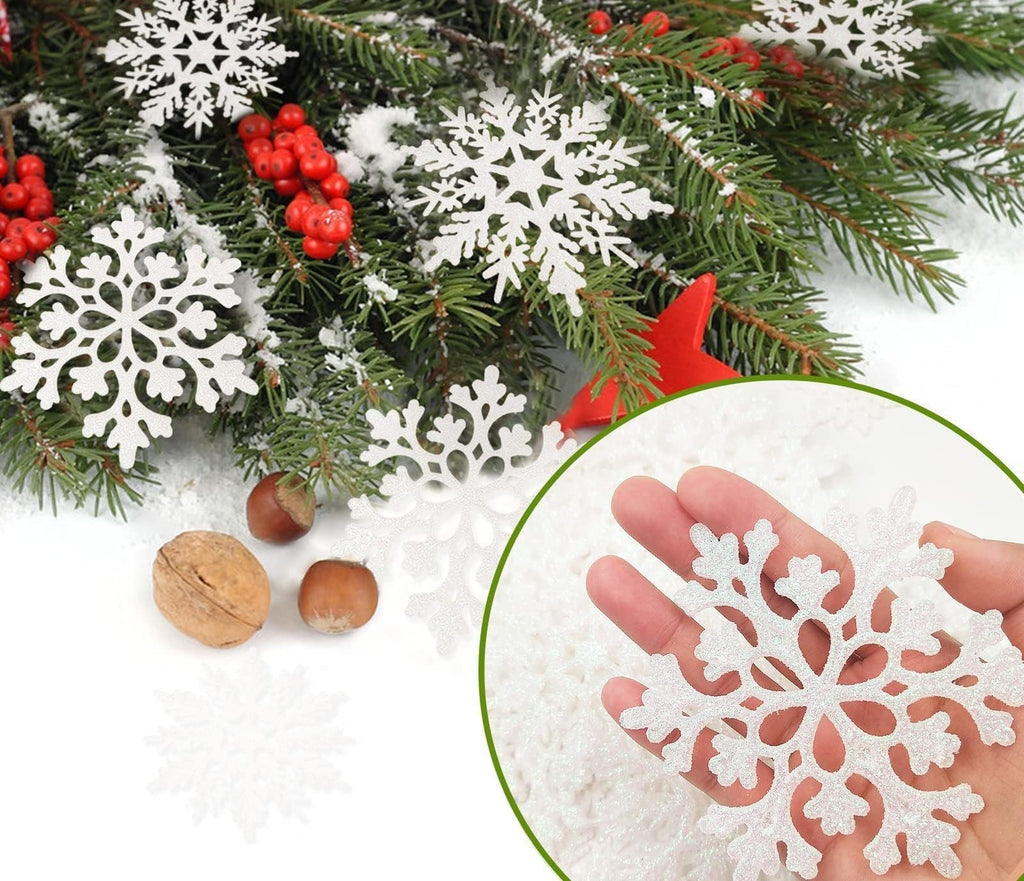 Hand holding a white glitter snowflake ornament with Christmas tree branches and berries in the background.