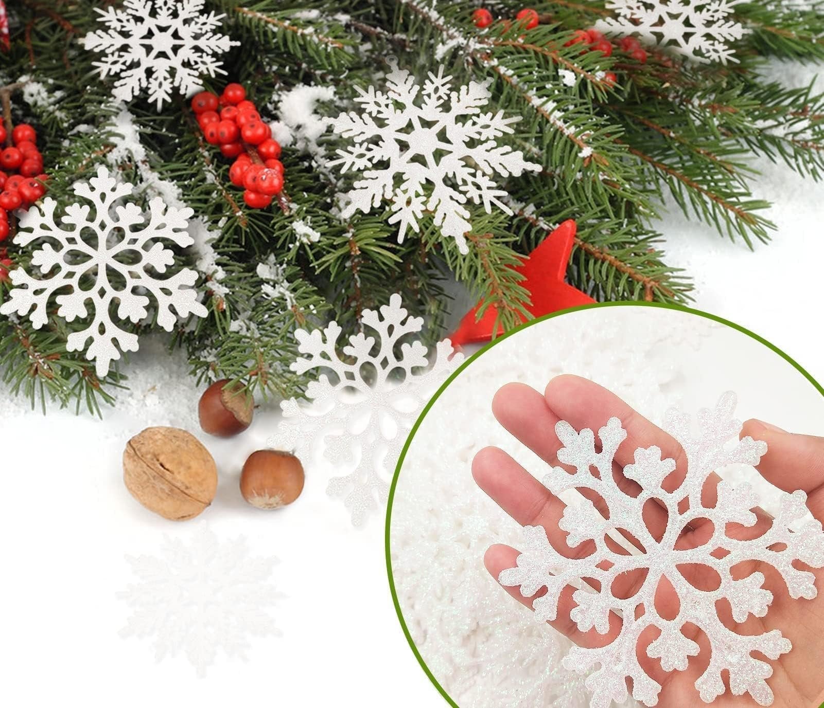 Hand holding a white glitter snowflake ornament with Christmas tree branches and berries in the background.