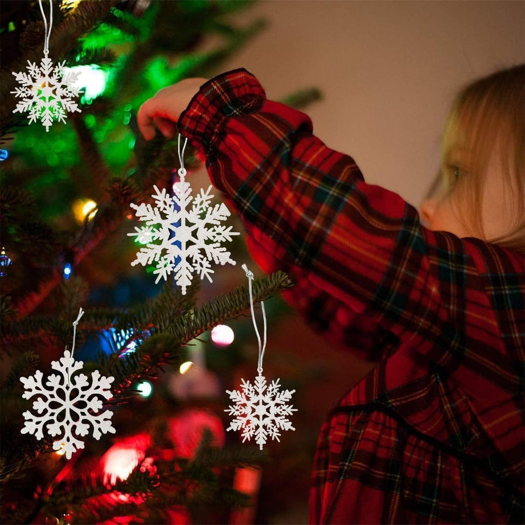 Child decorating a Christmas tree with white glitter snowflake ornaments, close-up on ornaments and sleeve.