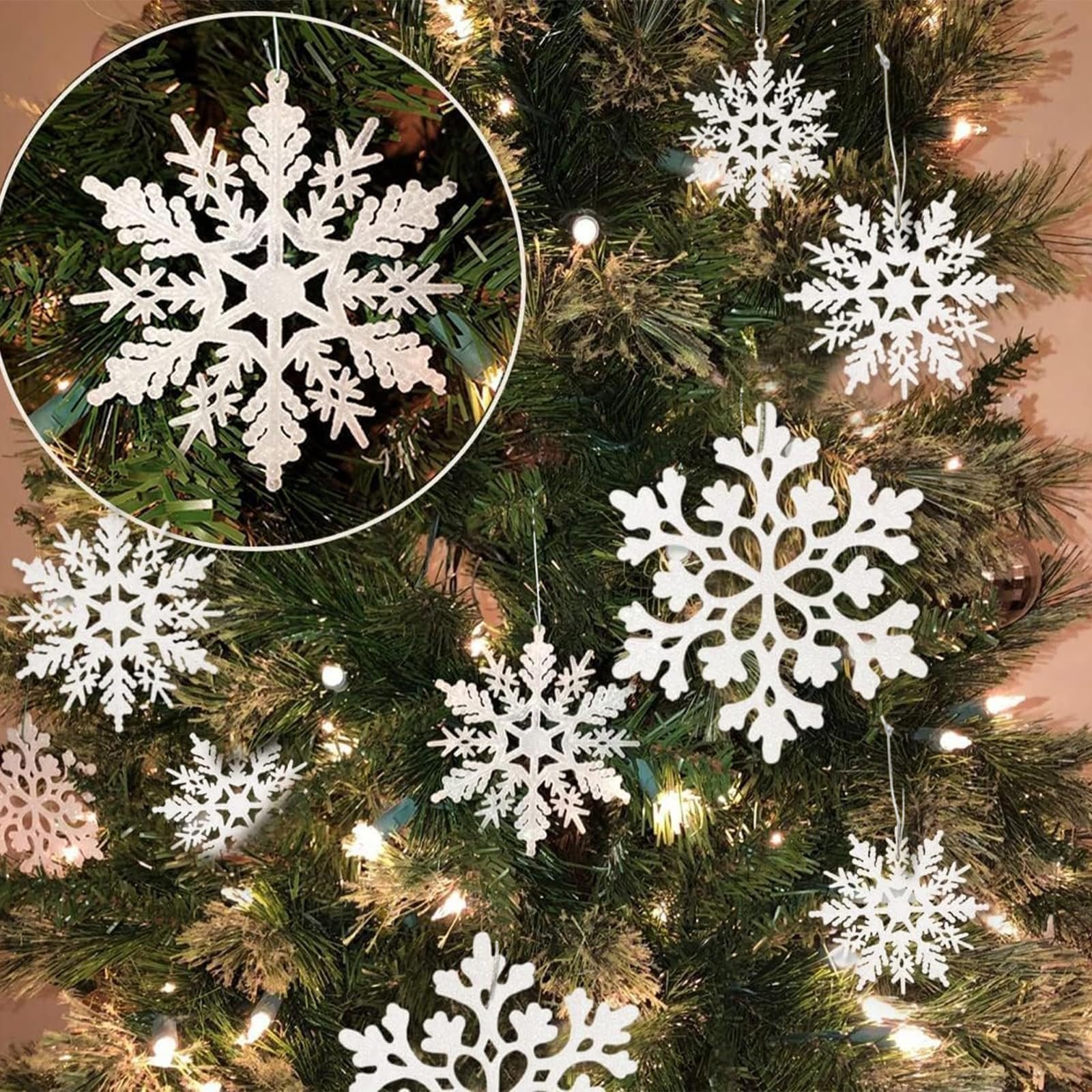 White glitter snowflake ornaments hanging on a Christmas tree with lights. Close-up inset shows one snowflake detail.