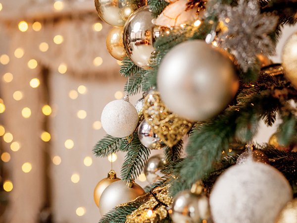Close-up of a Christmas tree branch adorned with wine red, gold, and silver shatterproof ball ornaments against a bokeh background of warm lights.
