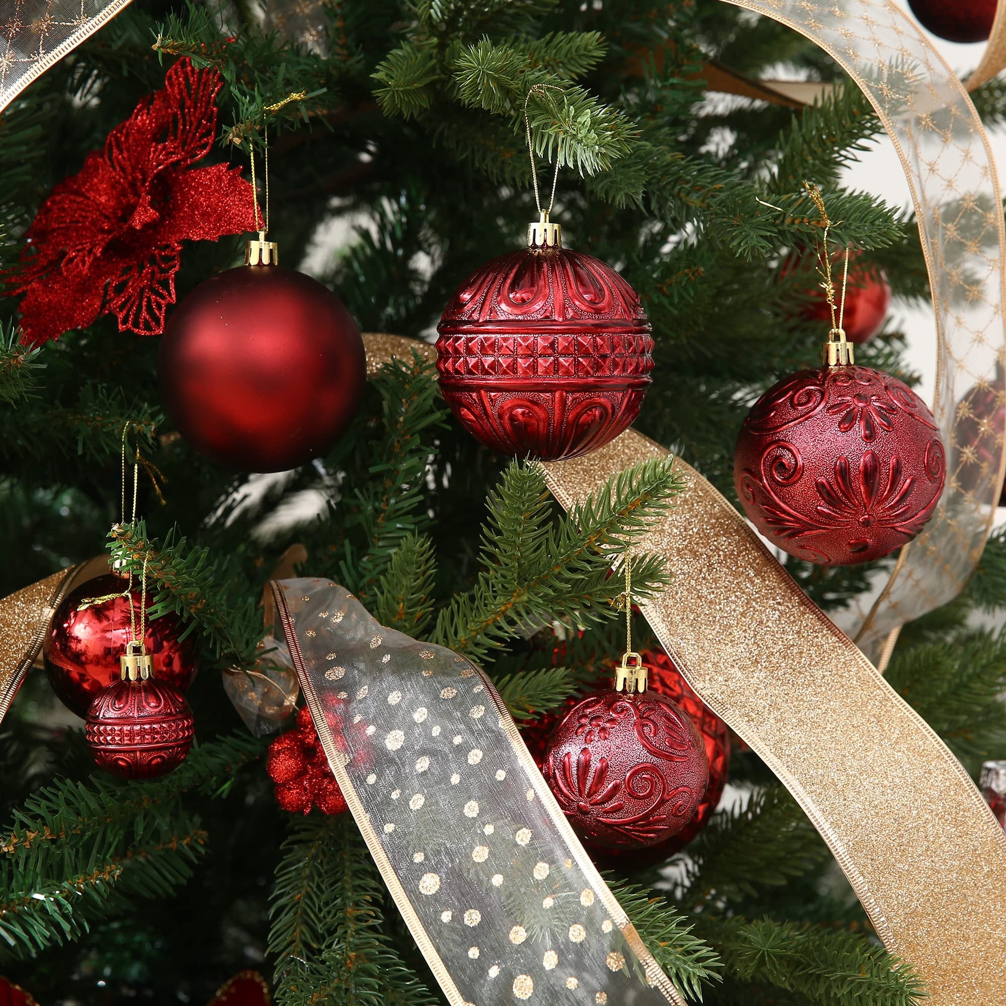 Close-up of red shatterproof Christmas ball ornaments hanging on a decorated tree with gold and patterned ribbons.