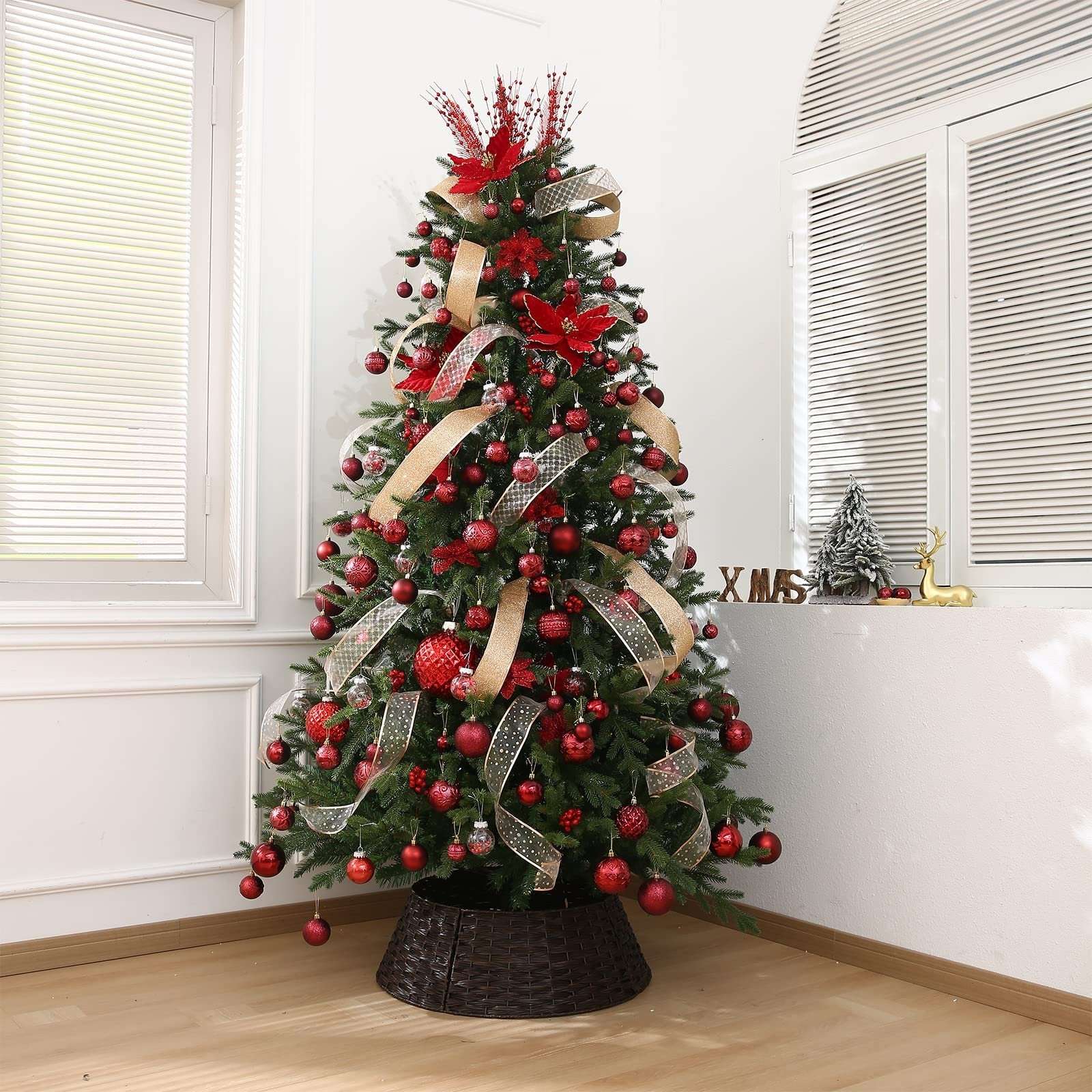 Decorated Christmas tree with red ornaments and gold ribbon, set in a room with windows.
