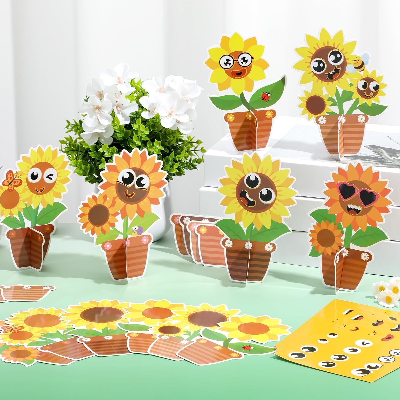 DIY sunflower craft kit pieces laid out with cartoon faces, pots, and stickers, next to a vase of white flowers.