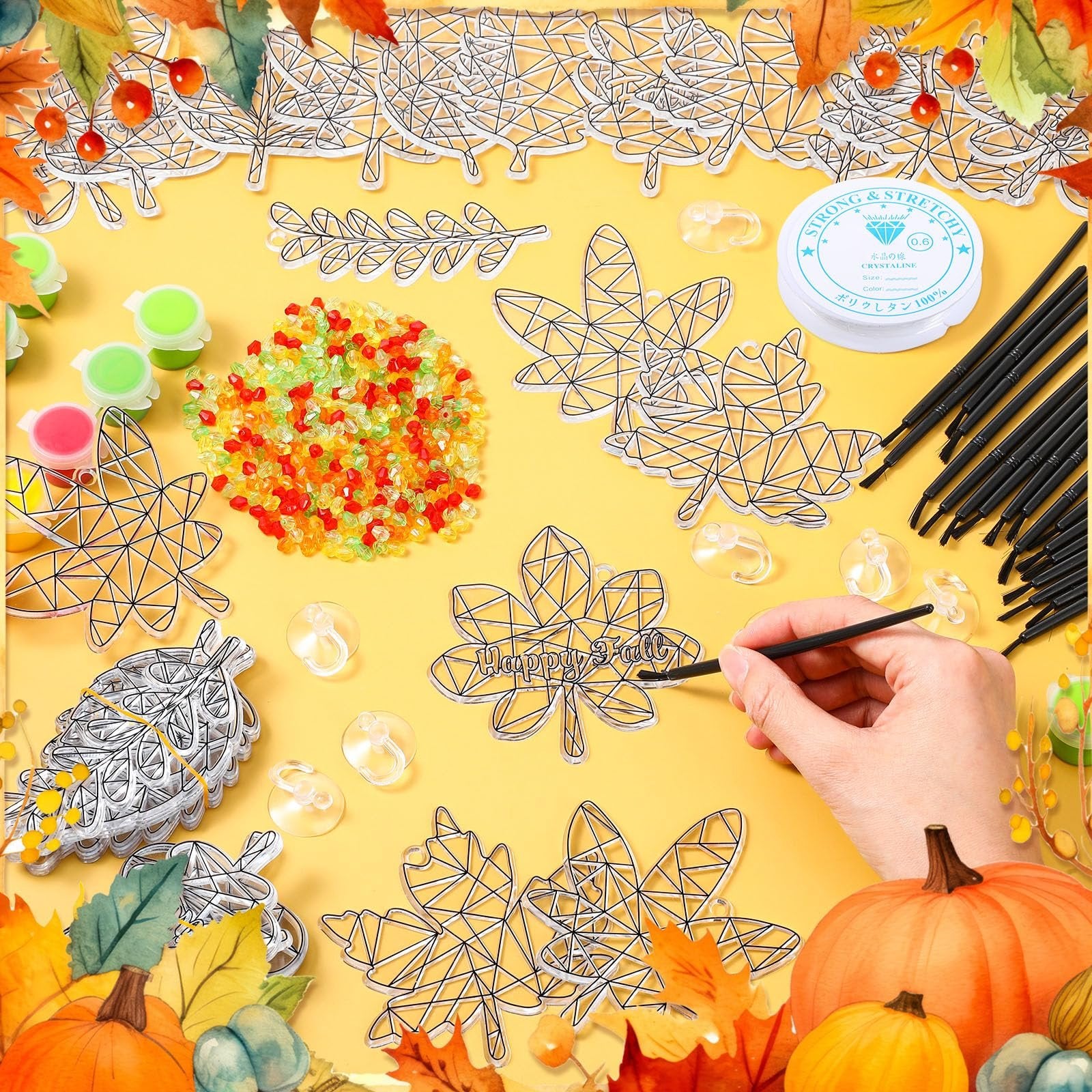 Pumpkin leaf suncatcher paint kit contents laid out on yellow background with autumn leaves border