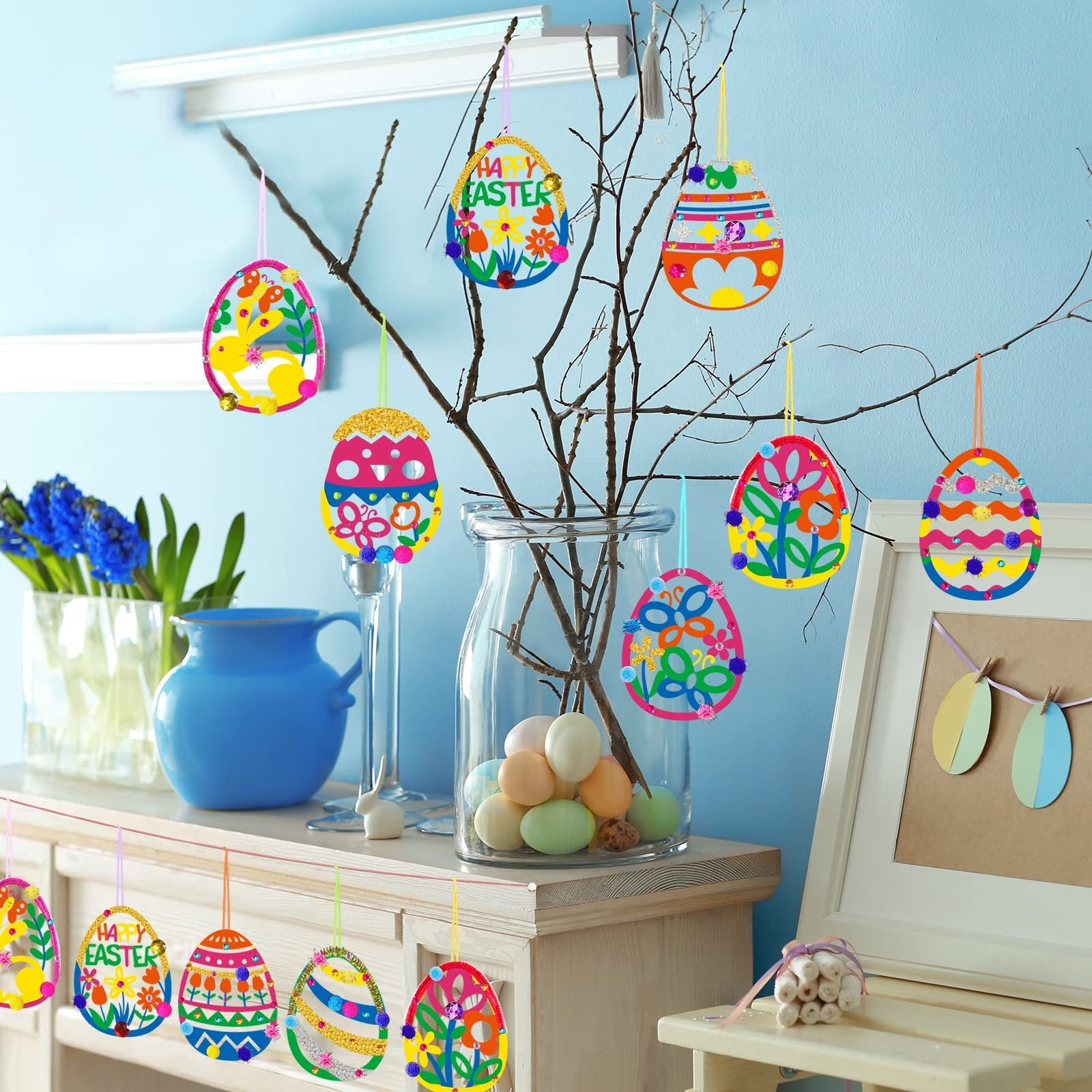 Easter egg ornaments hanging on branches, some with 'Happy Easter' text, decorated with glitter and pom-poms.