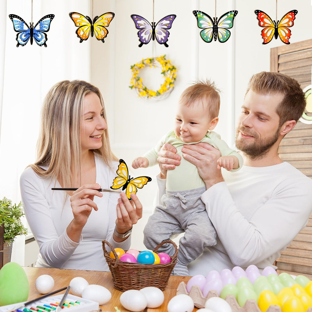 Family painting wooden butterfly ornaments for Easter, with colorful eggs and craft supplies on table.