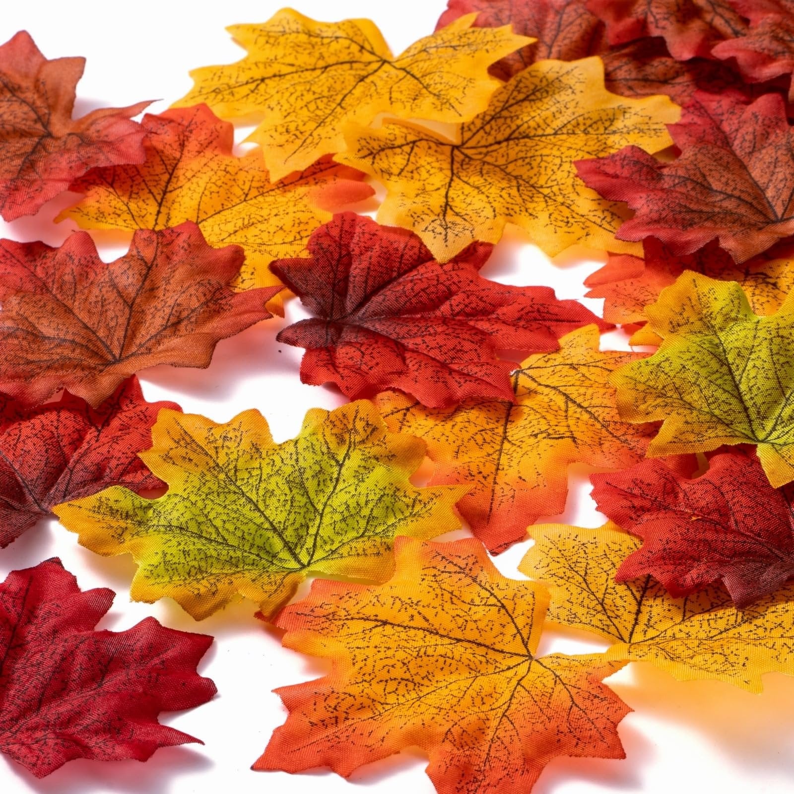 Pile of artificial maple leaves in red, orange, yellow, and green hues on a white background.