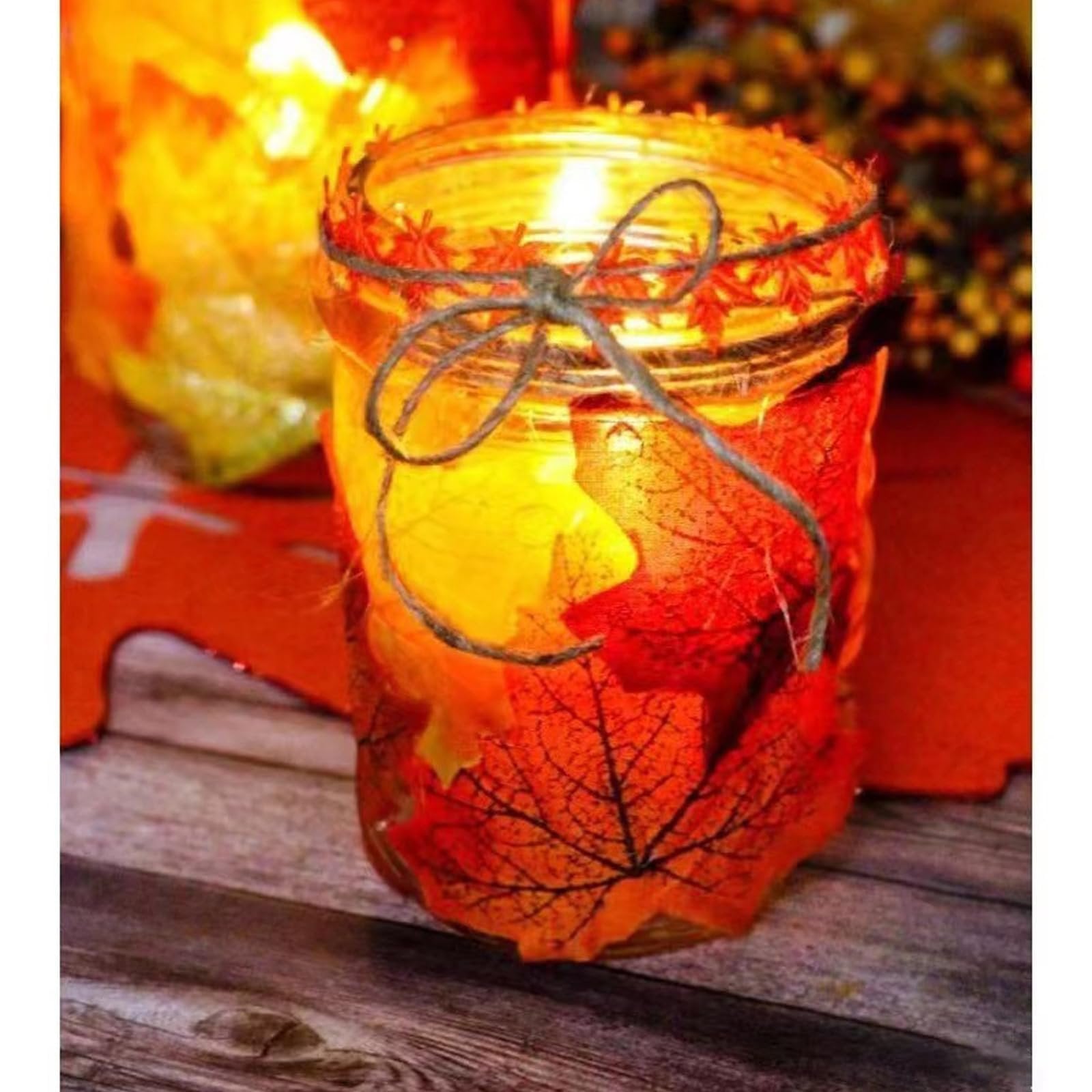 Close-up of a glass jar decorated with artificial maple leaves and twine, lit from within.