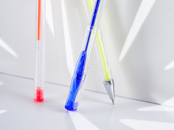 Close-up of three gel pens with red, blue, and yellow ink, angled on a white surface with light shadows.