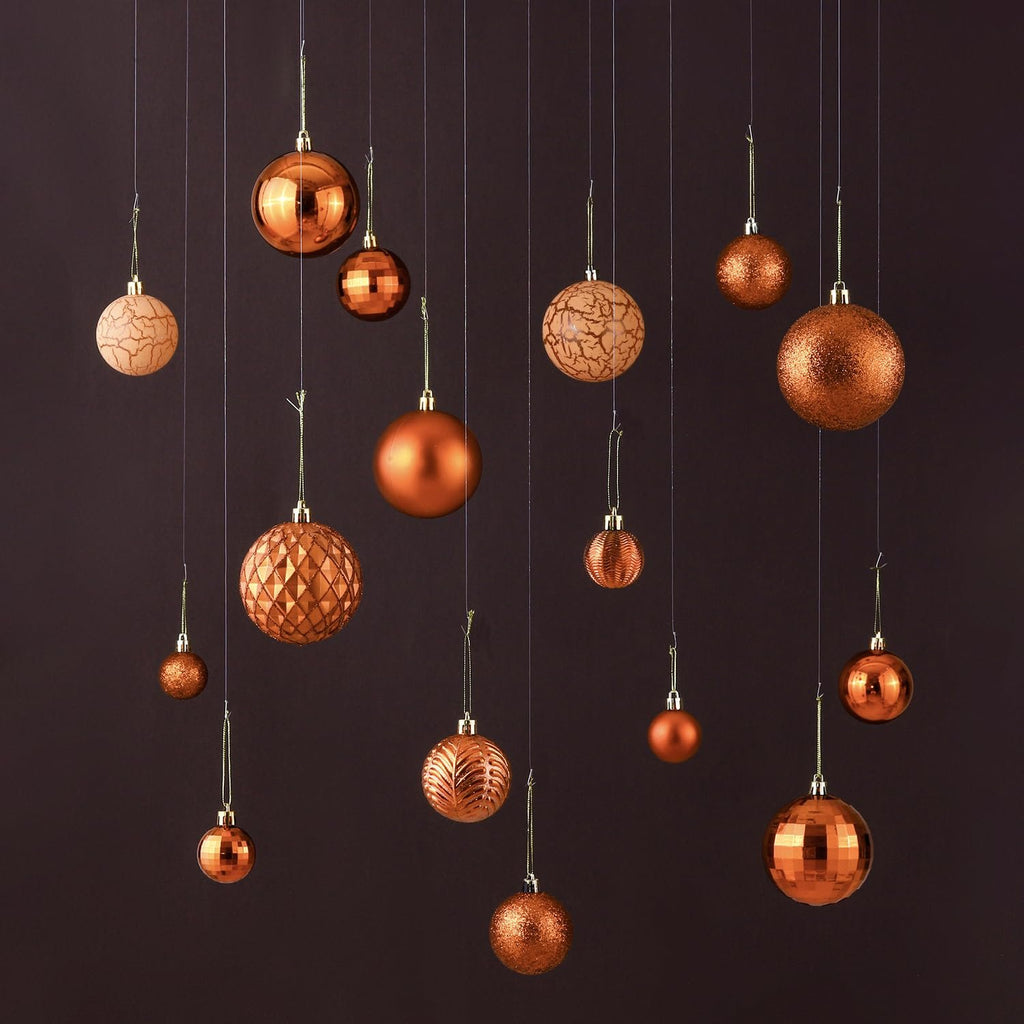 Assortment of copper orange Christmas ball ornaments in various sizes and styles hanging against a dark background.