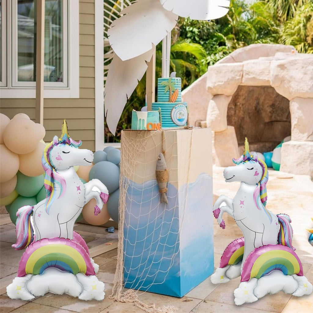 Two standing unicorn foil balloons with rainbow and cloud bases at a party decoration setup.