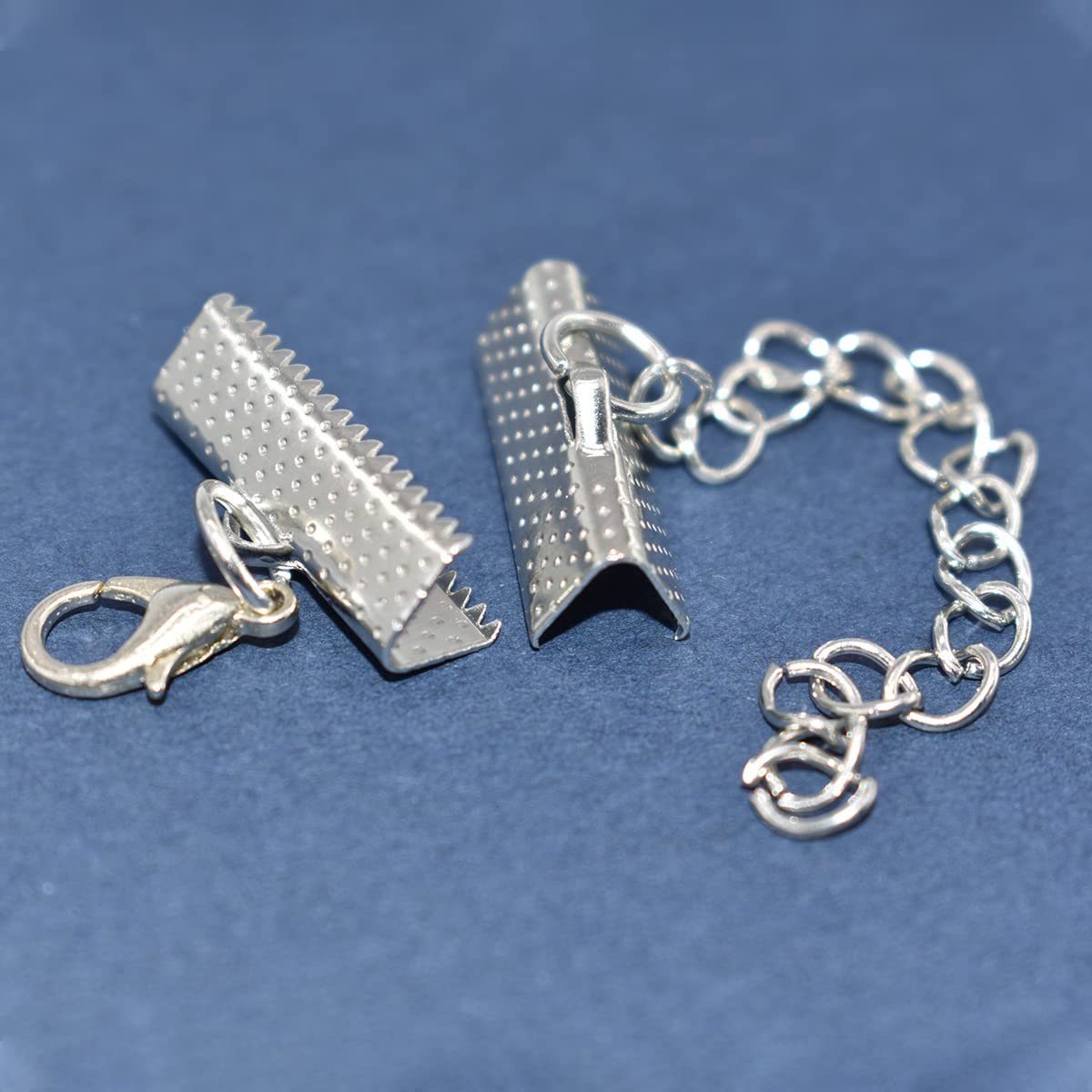 Silver ribbon end clasps with lobster clasp and chain extender on blue background