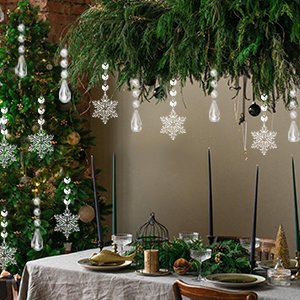 Acrylic snowflake and icicle drop ornaments hanging from greenery above a decorated table and Christmas tree.