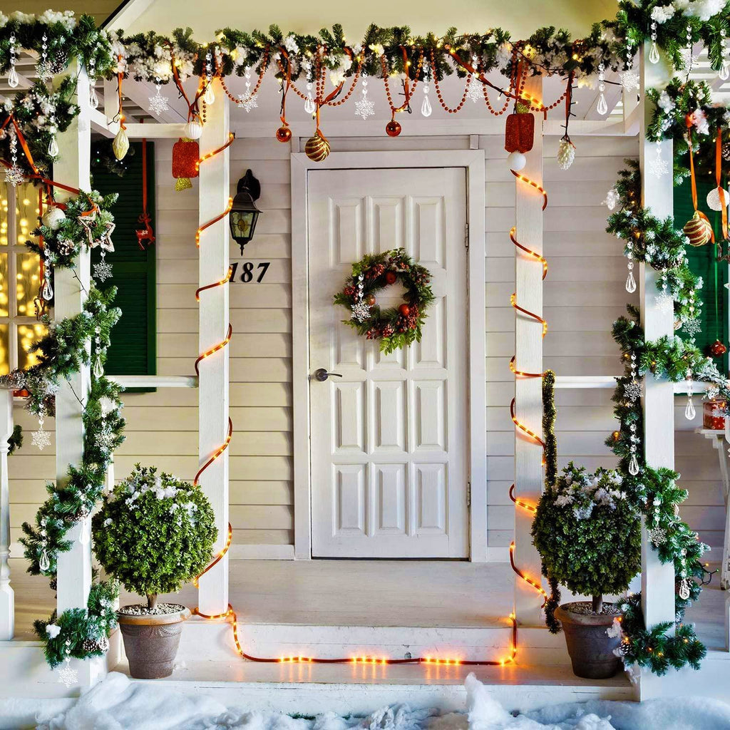 Front porch decorated for Christmas with garlands, lights, and ornaments on a white door and siding.