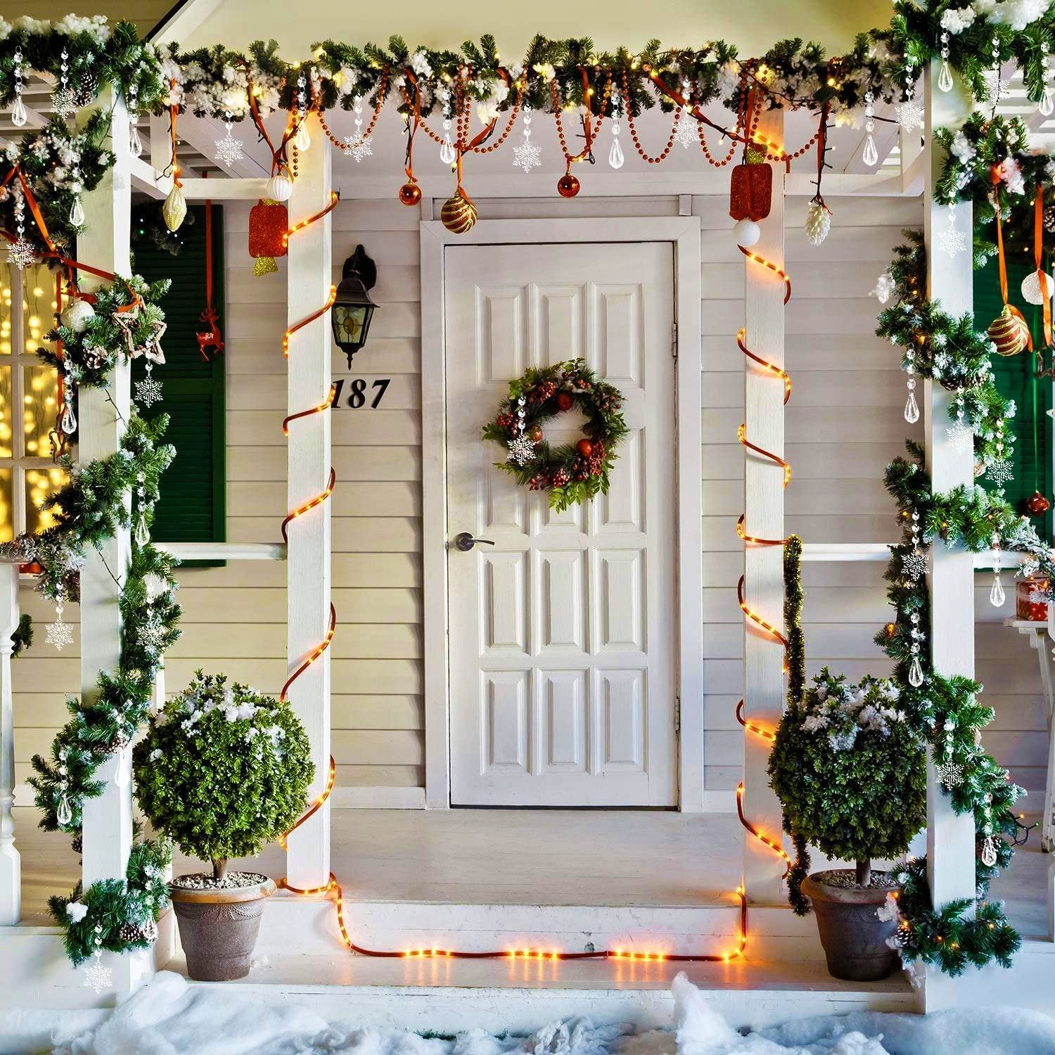 Front porch decorated for Christmas with garlands, lights, and ornaments on a white door and siding.