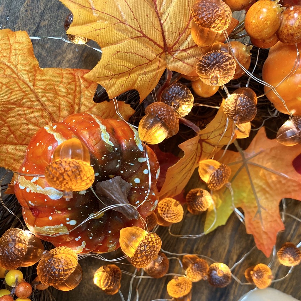 Close-up of fall harvest string lights with acorn-shaped LEDs, artificial leaves, and a small pumpkin.