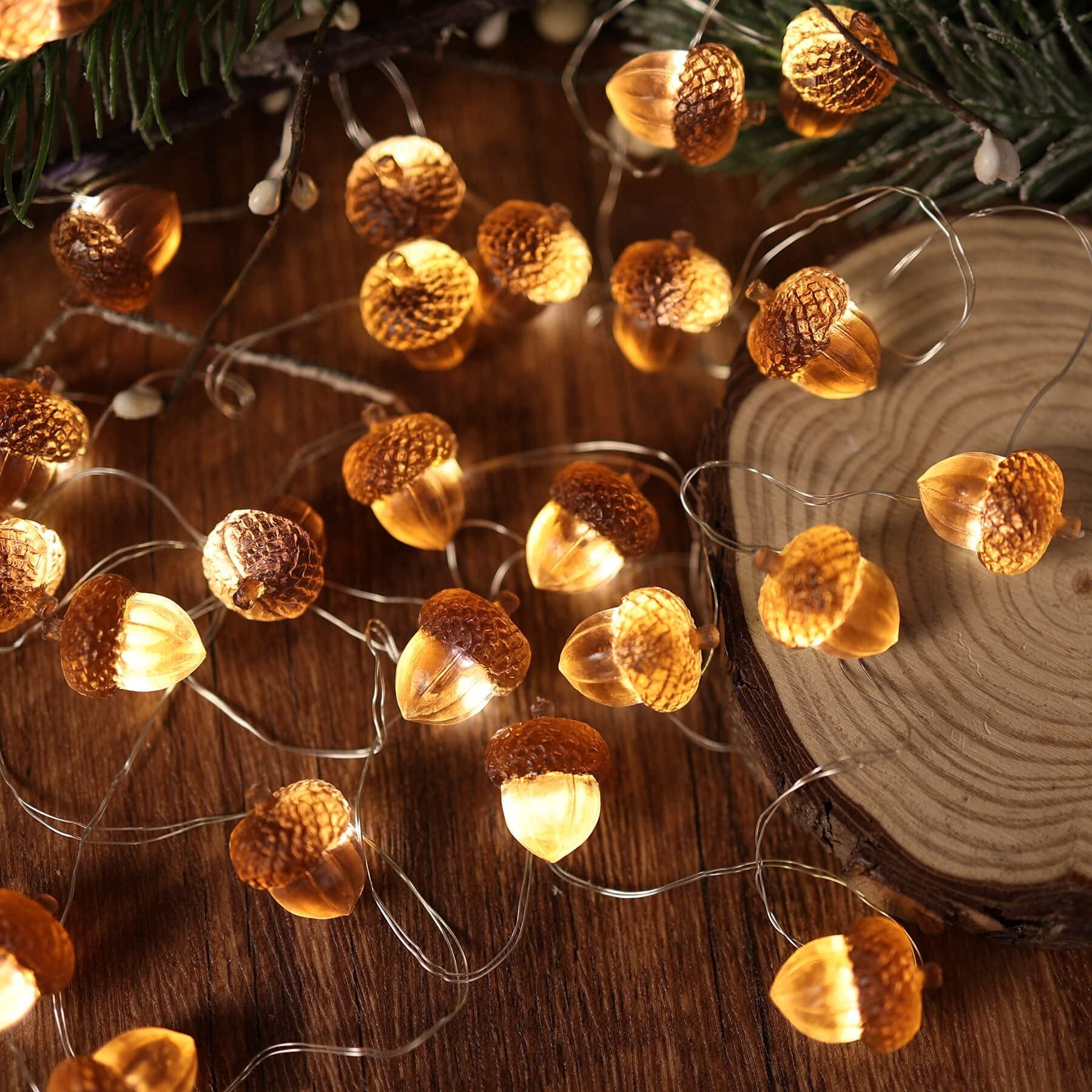 String lights shaped like acorns with warm LED lights on a wooden surface with pine branches.