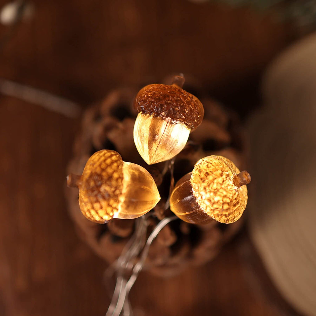 Three illuminated acorn-shaped string lights close-up, with a pinecone in the background.